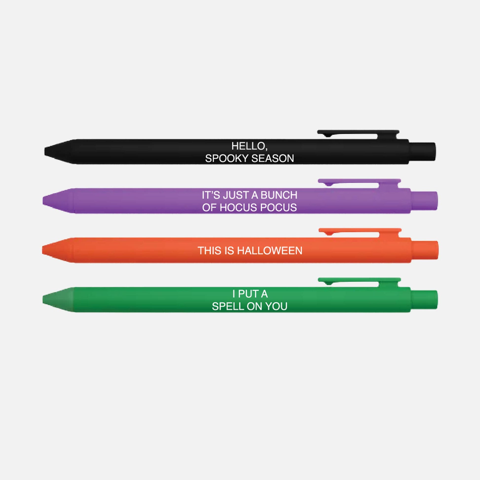Four novelty ballpoint pens in black, purple, orange, and green, arranged vertically on a white background. Each pen has a white printed phrase related to Halloween: 'HELLO, SPOOKY SEASON', 'IT'S JUST A BUNCH OF HOCUS POCUS', 'THIS IS HALLOWEEN', and 'I PUT A SPELL ON YOU'.