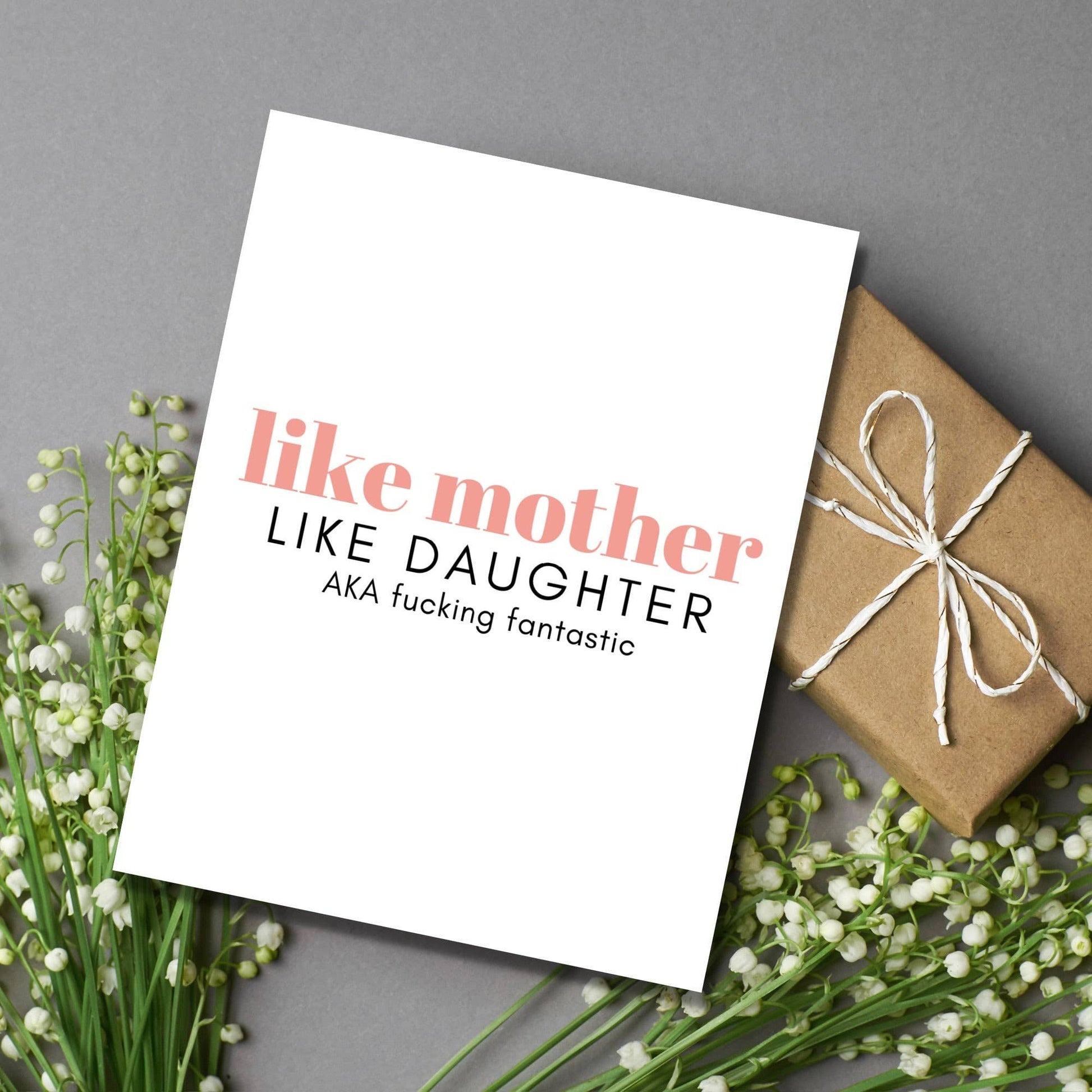 Greeting card with 'like mother like daughter' text, wrapped gift, and flowers on a gray background