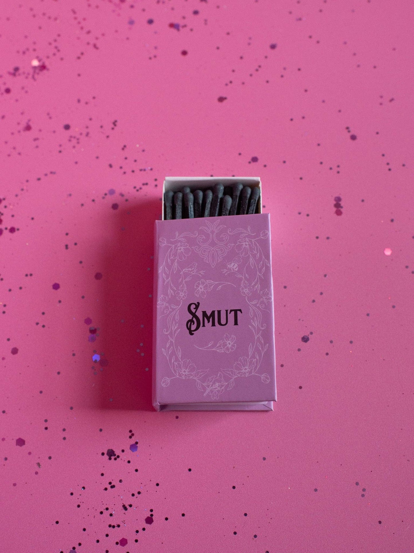 Matchbox labeled 'Smut' on a pink background with confetti