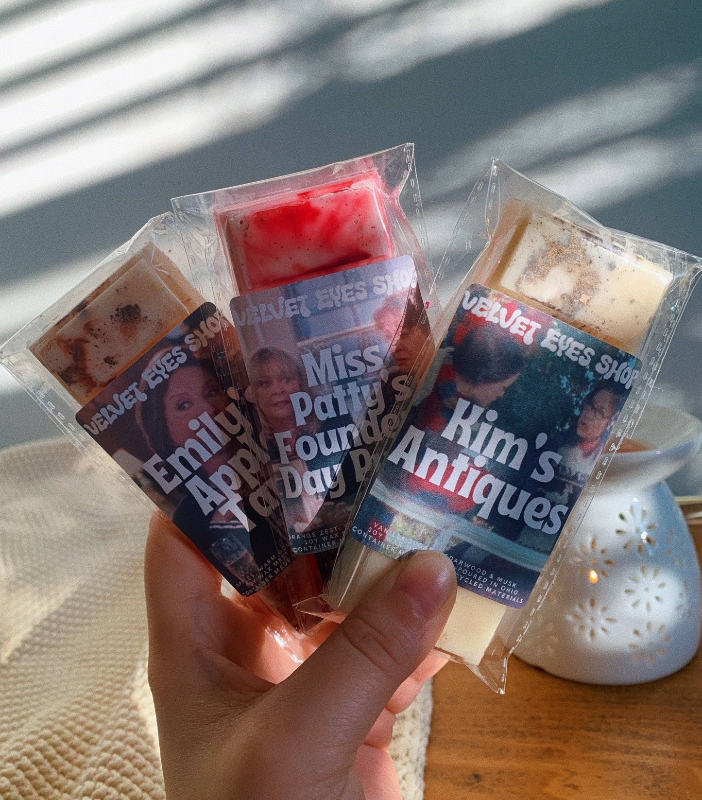 Three small candles in clear packaging with printed labels held by a hand.