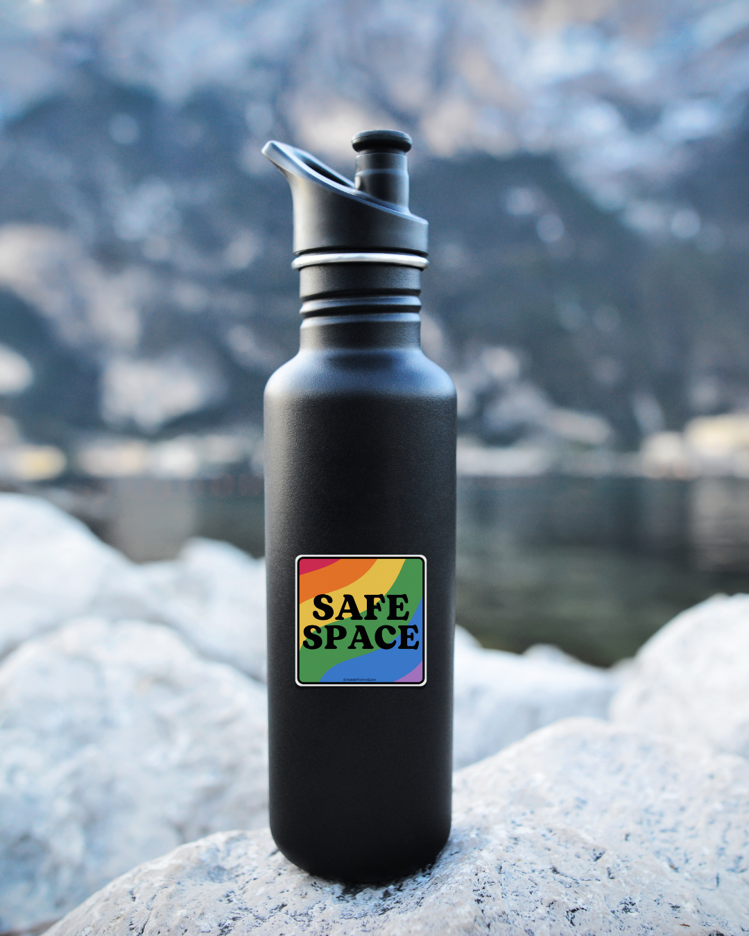 Black water bottle with a rainbow 'SAFE SPACE' sticker on a snowy background