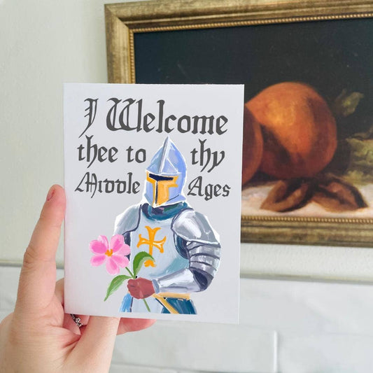 Card with a knight holding flowers and text 'I Welcome thee to thy Middle Ages' held by a hand, with a painting in the background.