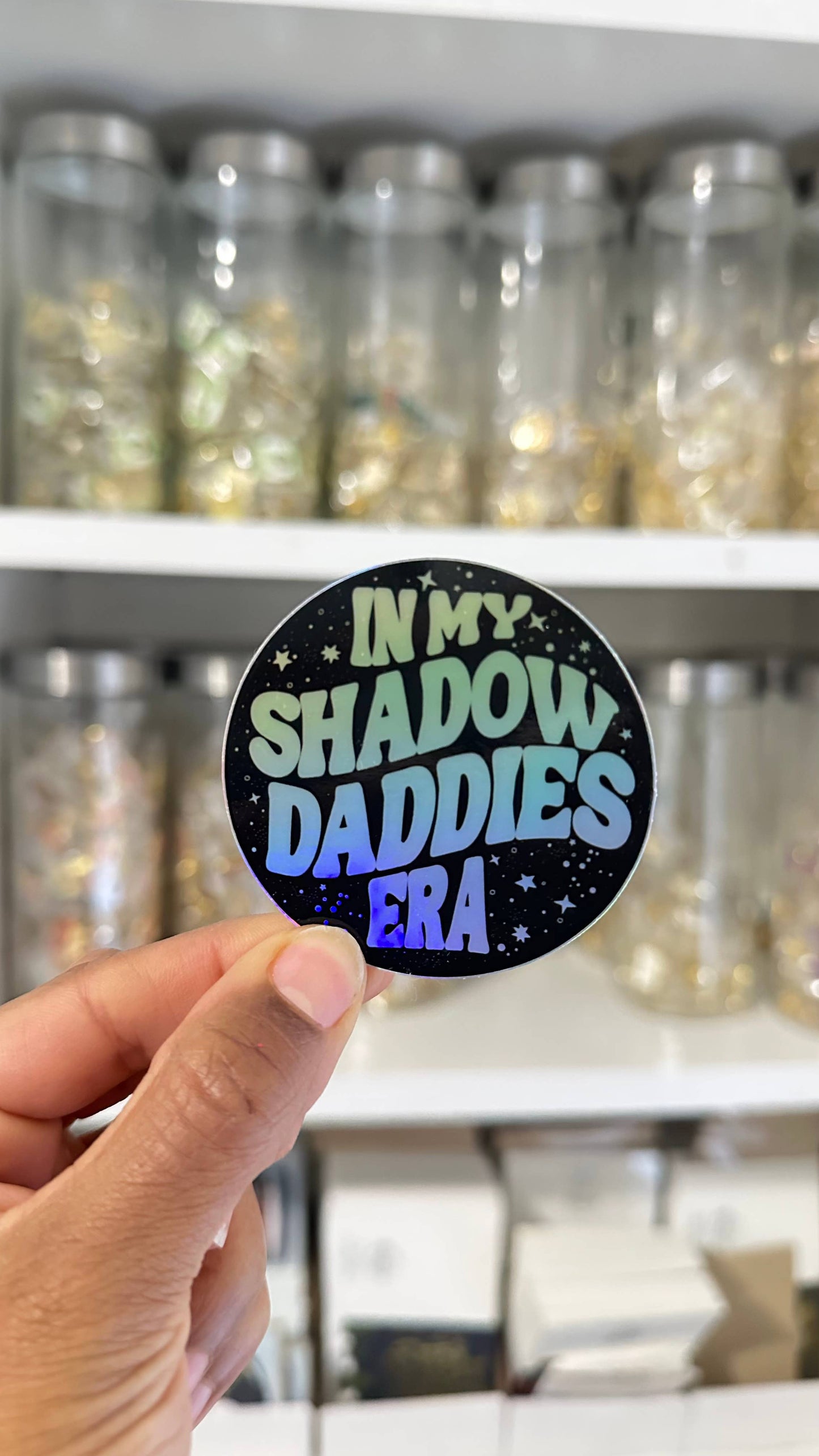Person holding a round sticker with text in front of shelves with jars.