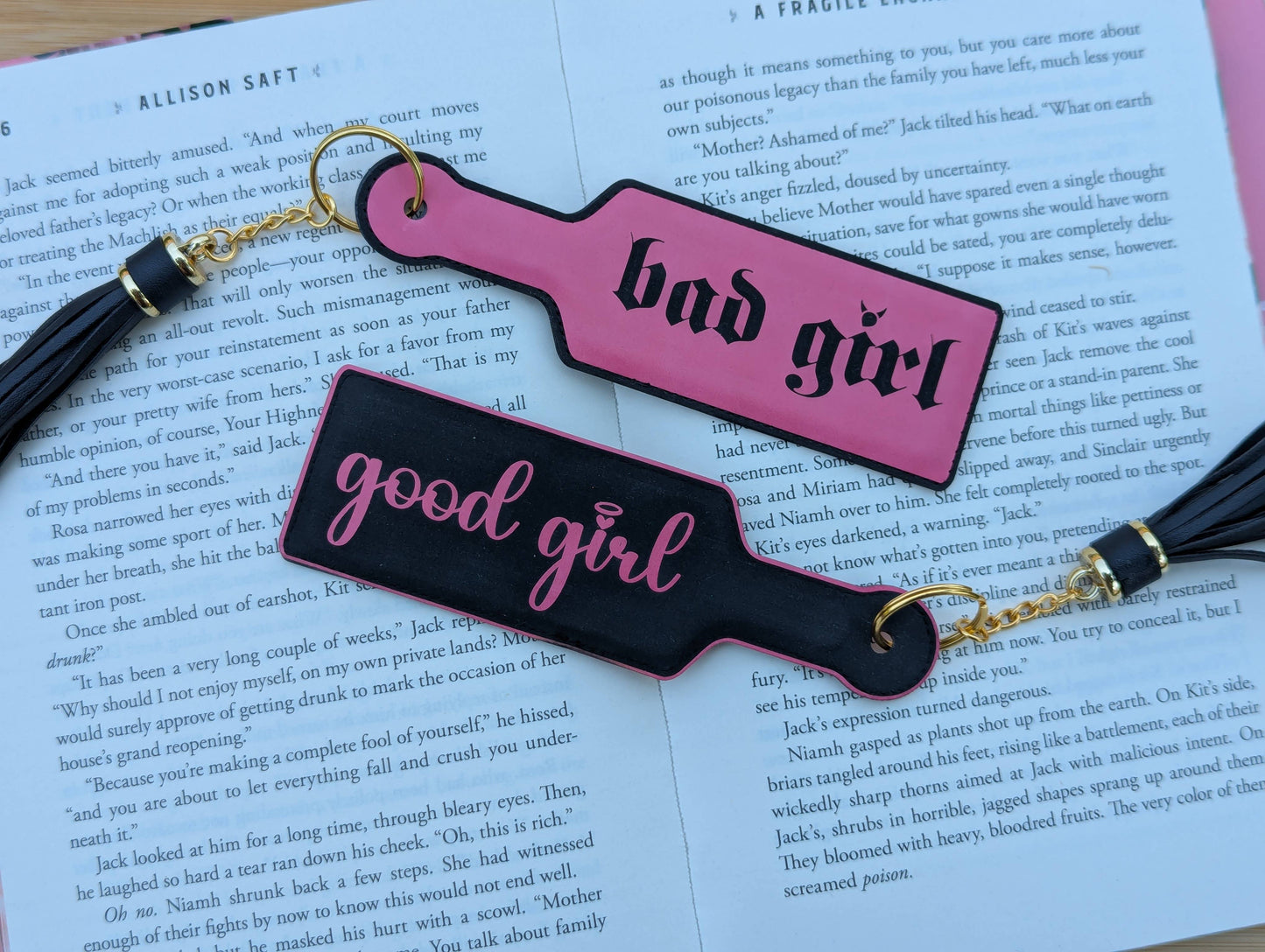 Two paddle-shaped keychains labeled 'bad girl' and 'good girl' on a book page.