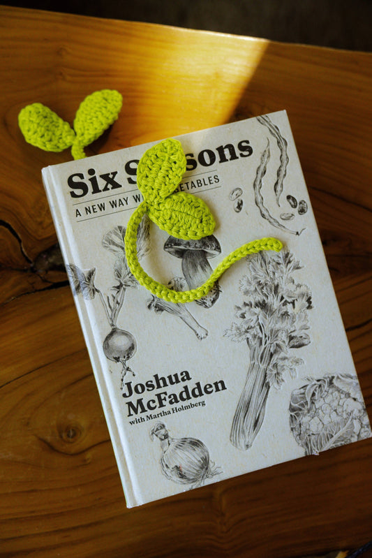 Book titled 'Six Seasons' by Joshua McFadden with a green knitted bookmark on a wooden surface.