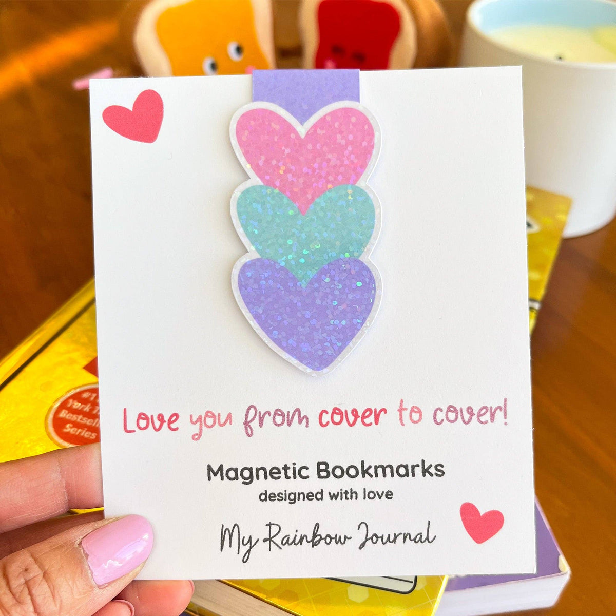 Magnetic bookmarks with heart designs on a card held by a hand.