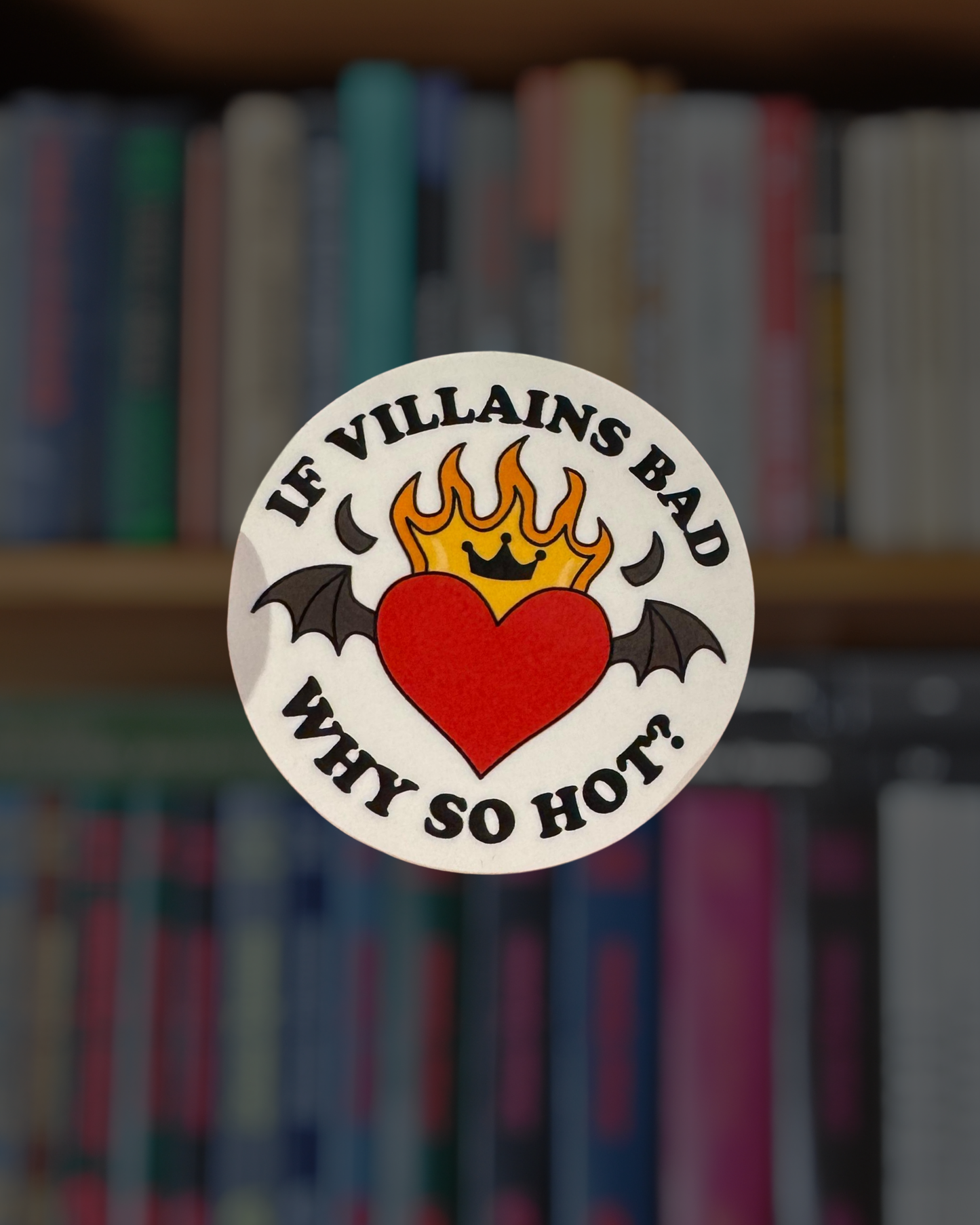 Sticker with a heart and bat design on a blurred bookshelf background
