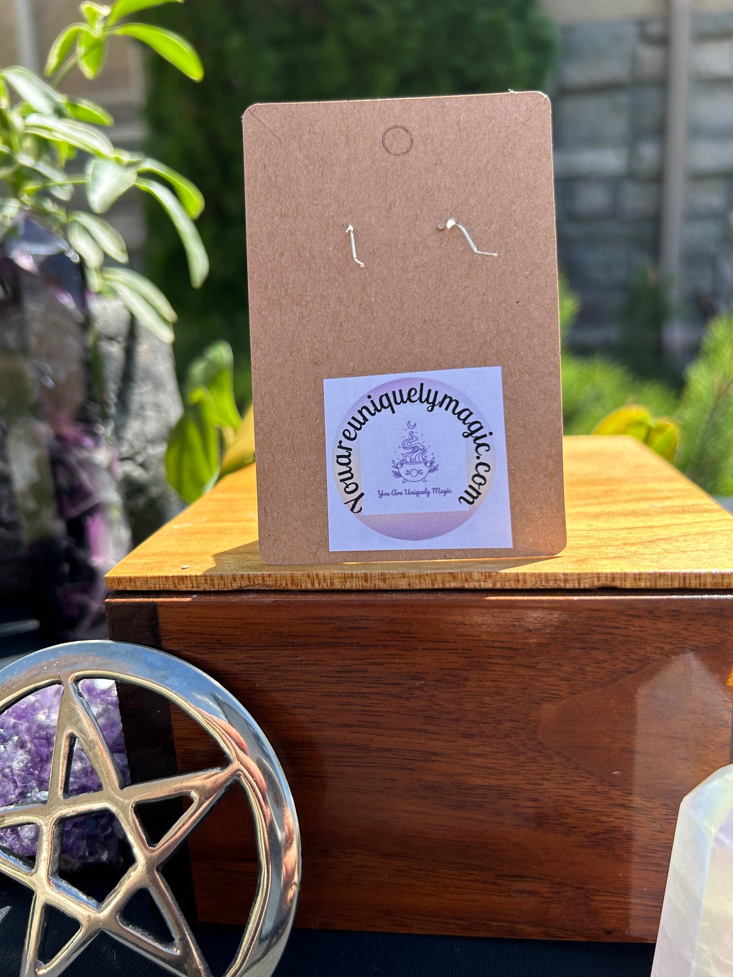 Earring card with 'uniquelymagic.com' label on a wooden surface with a pentacle symbol in the foreground.