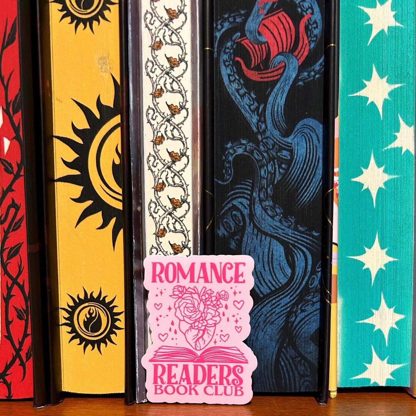 Colorful book spines with decorative designs and a 'Romance Readers Book Club' sign in front.