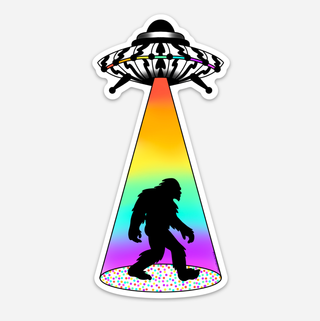 A die-cut sticker featuring a black silhouette of Bigfoot walking under a rainbow-colored spotlight beam directed upward by a black-and-white flying saucer, on a light gray background.