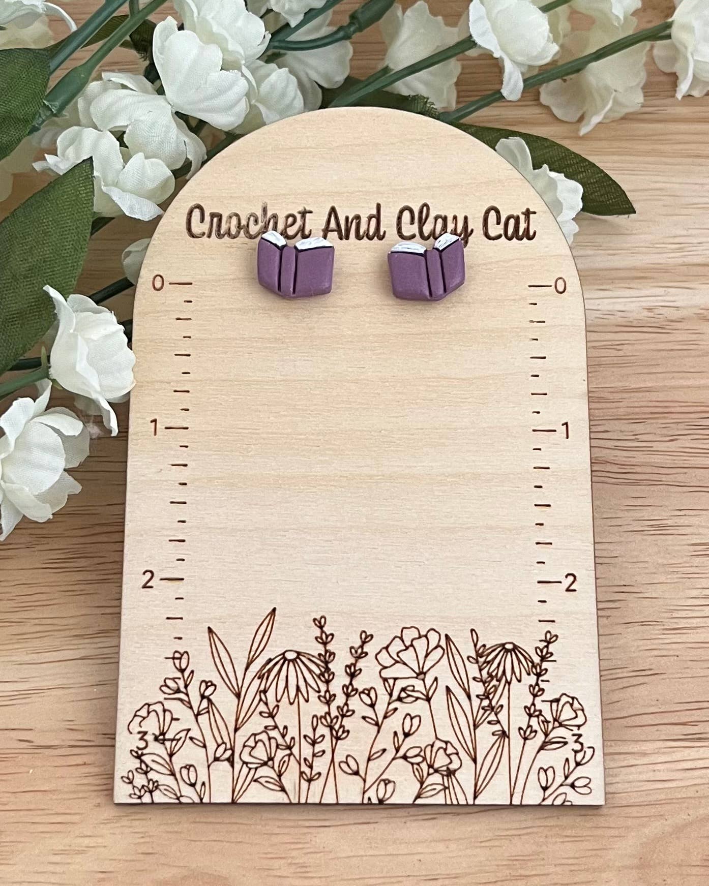 Purple earrings on a wooden card with floral design, surrounded by white flowers.