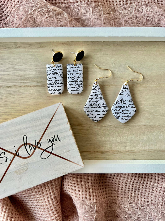 Pair of earrings with script design on a wooden surface with a card reading 'I love you'.