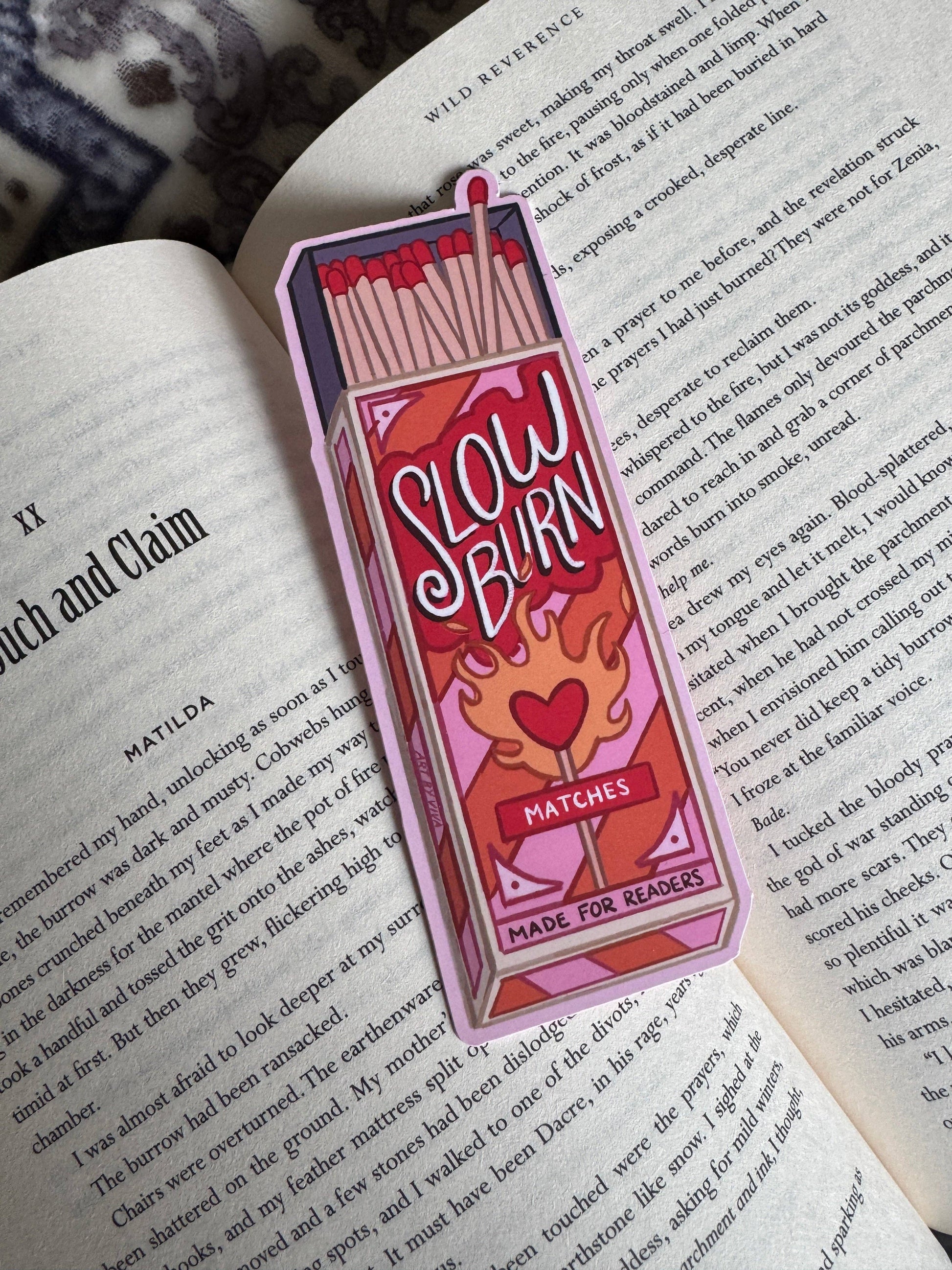 Bookmark shaped like a matchbox with 'Slow Burn Matches' design on an open book.
