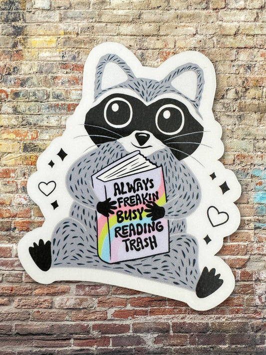 Sticker of a raccoon holding a book with text on a brick wall background
