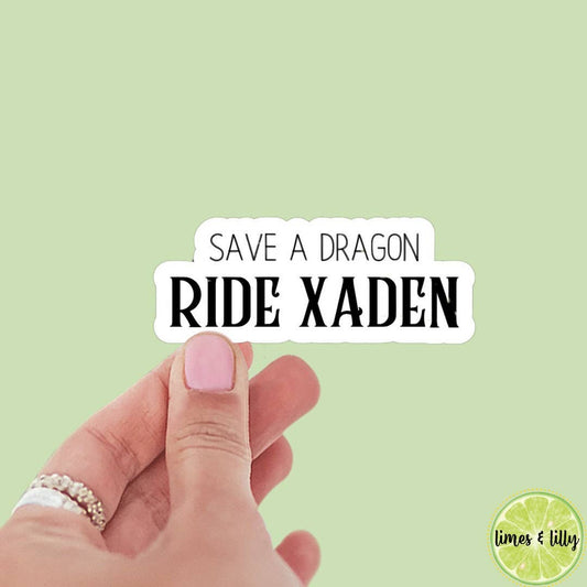 Hand holding a sticker with 'Save a Dragon Ride Xaden' text on a light green background