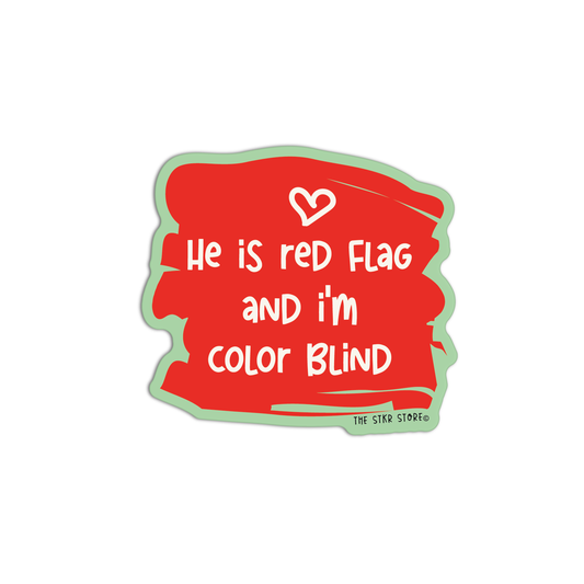 A die-cut sticker with a red paint-splatter background, white text reading 'He is red flag and i'm color blind', a small white heart, and a light green outline, shown on a plain white background. Small text at the bottom right reads 'THE STAR STORE co'.