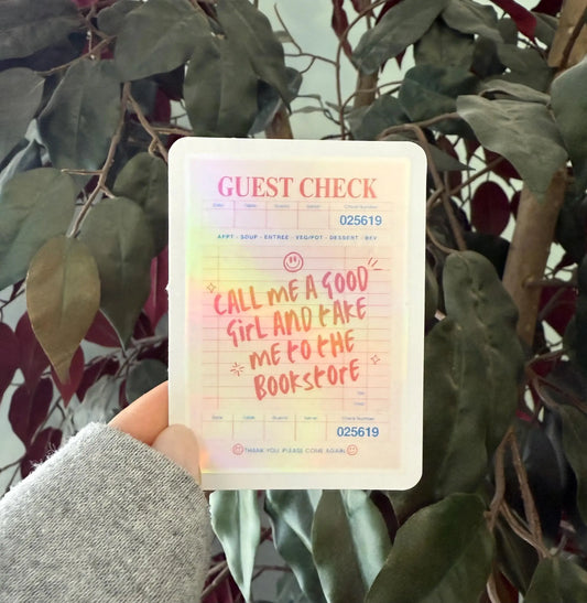 Card with text 'Call me a good girl and take me to the bookstore' held in front of green leaves