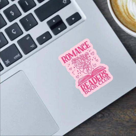 Pink 'Romance Readers Book Club' sticker on a laptop keyboard with a cup of coffee in the background.