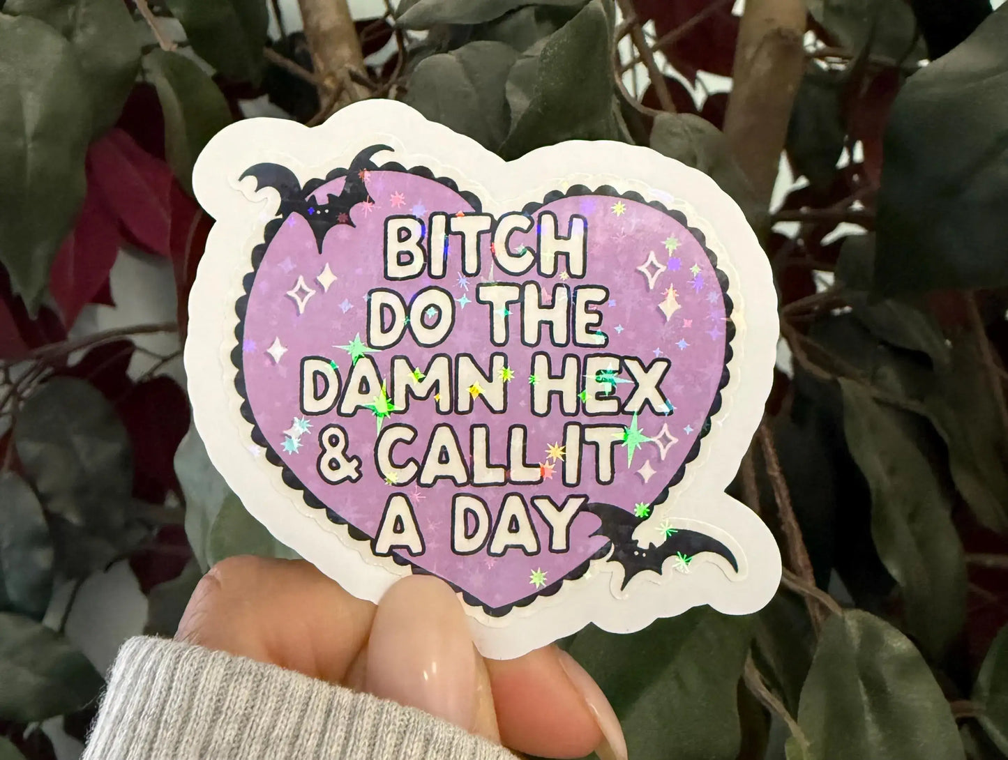 Heart-shaped sticker with text held in front of green leaves