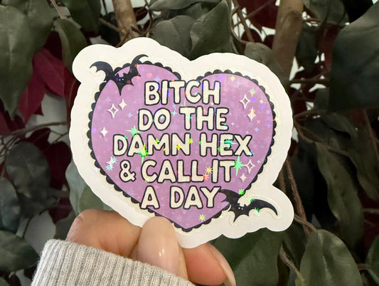 Heart-shaped sticker with text held in front of green leaves
