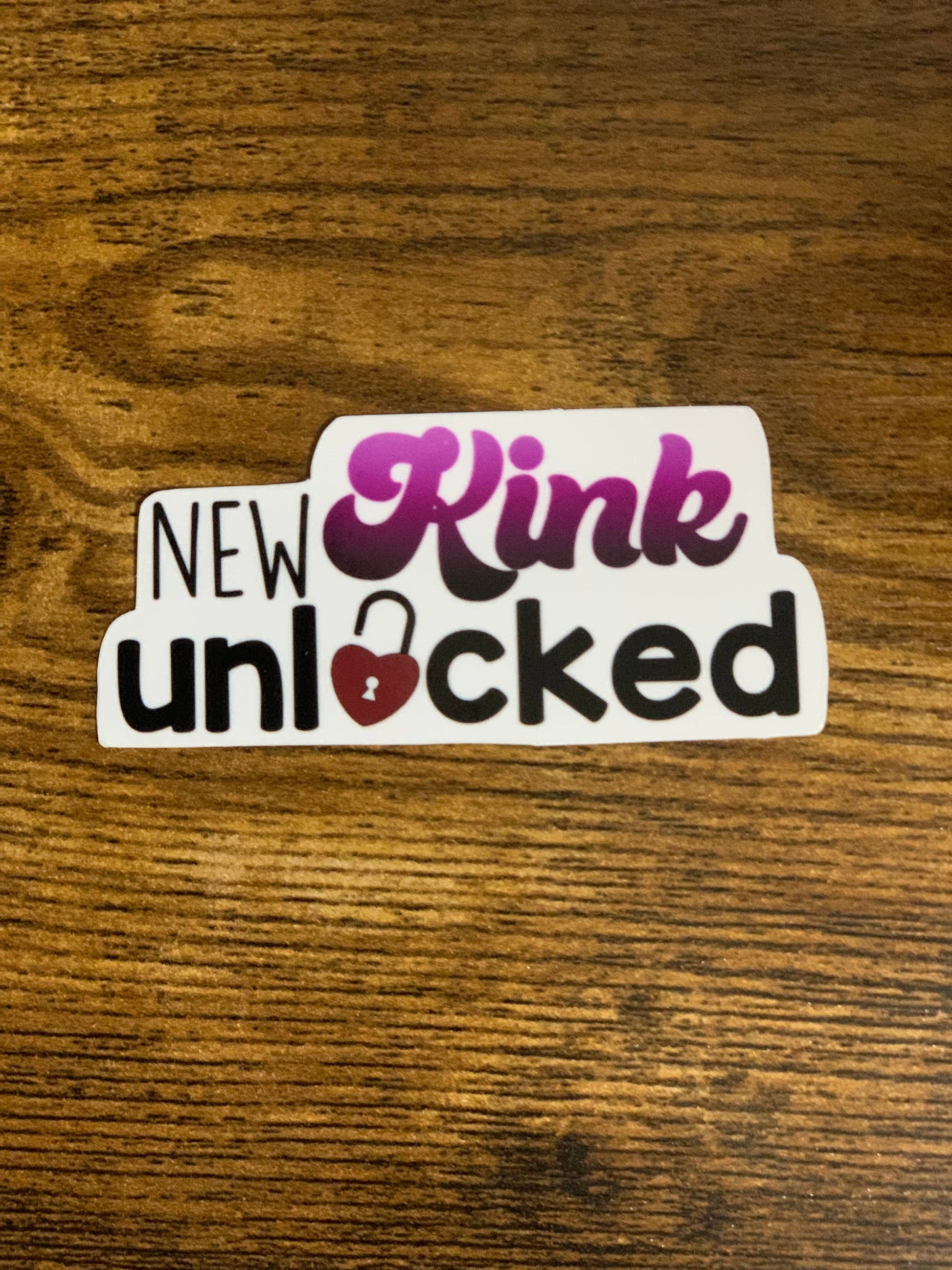 Sticker with 'New Kink Unlocked' text on a wooden surface