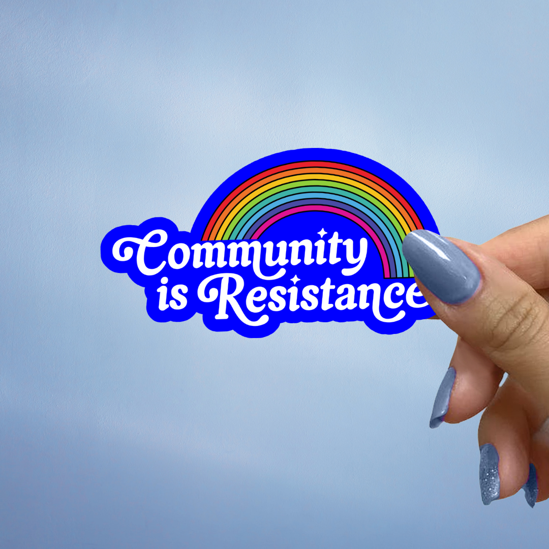 Sticker with rainbow and 'Community is Resistance' text held by a hand against a light blue background