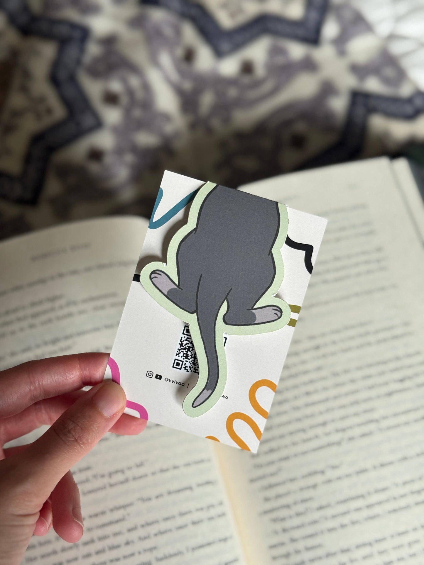 Hand holding a card with a cat illustration on a book background