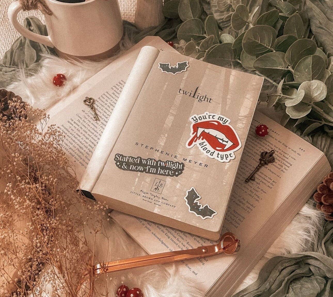 Open book with 'Twilight' stickers on a decorative surface with a mug and flowers.