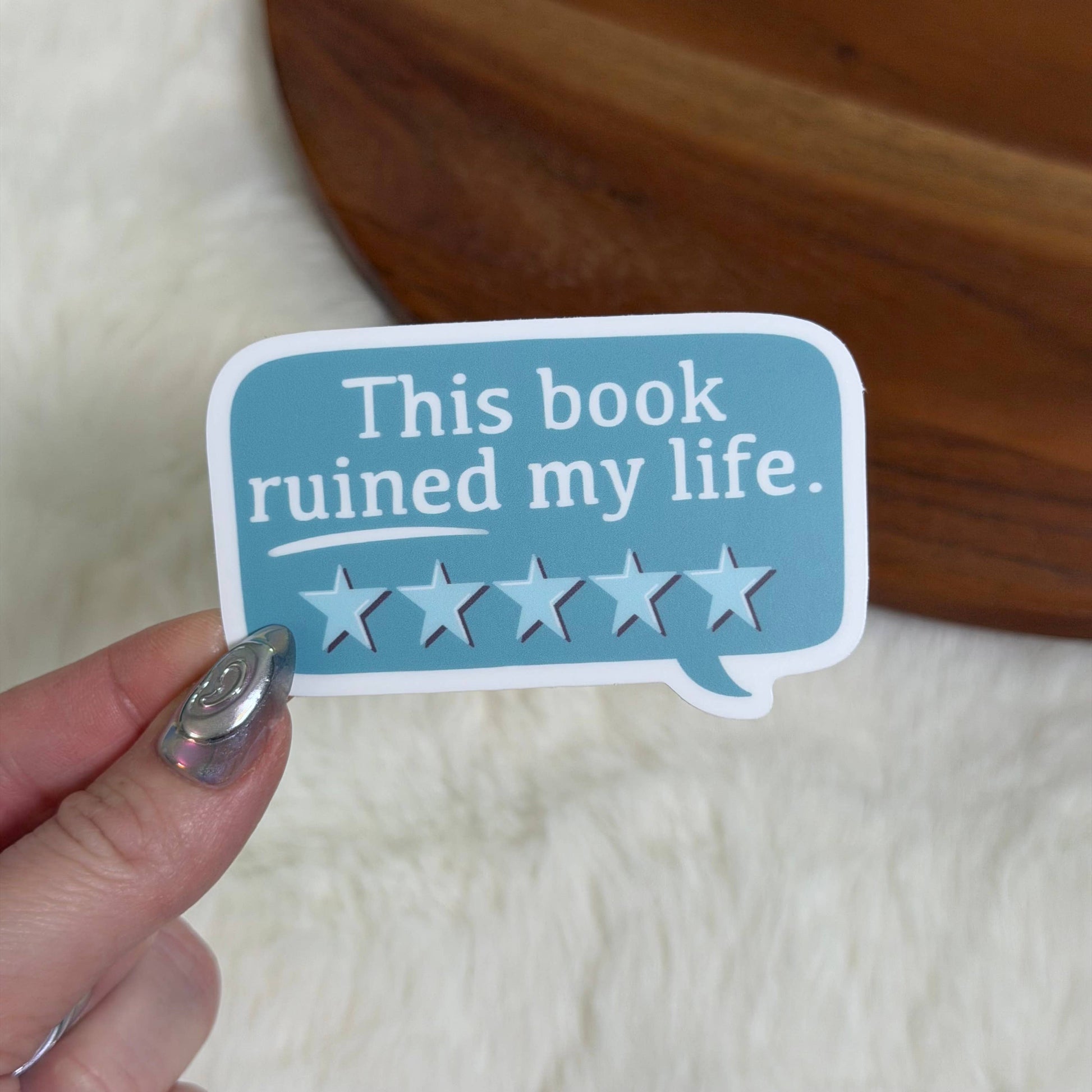 Sticker with 'This book ruined my life' text and star ratings held by a hand.