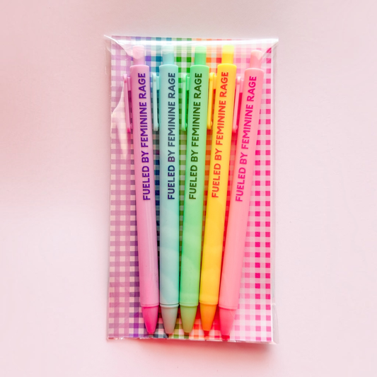A set of six colorful gel pens in a clear plastic sleeve with a pink and white gingham patterned backing. The pens are labeled 'FUELED BY FEMININE RAGE' in vertical text and come in shades of purple, blue, green, yellow, orange, and pink.