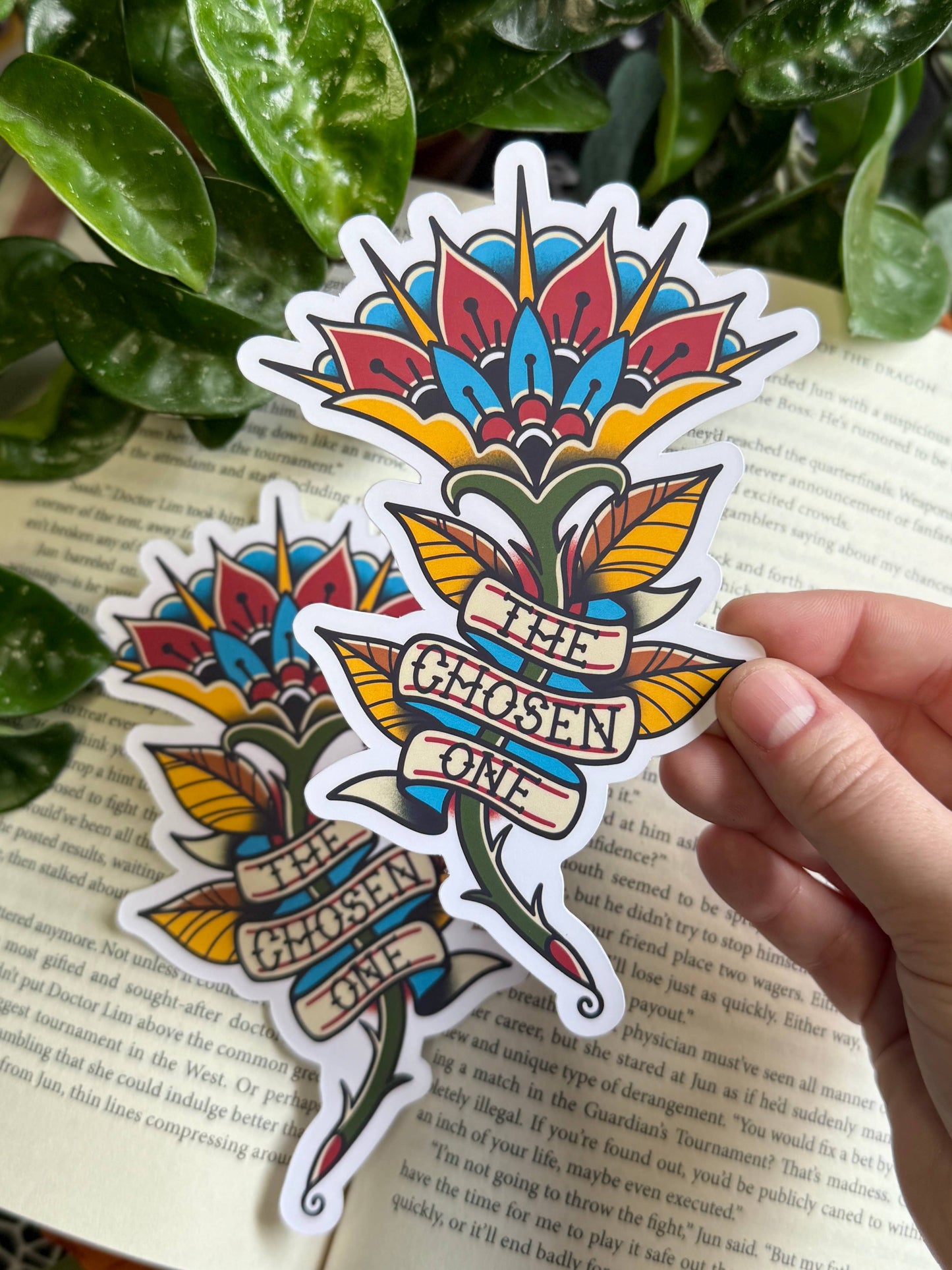 Colorful flower-shaped sticker with 'The Chosen One' text held over a book