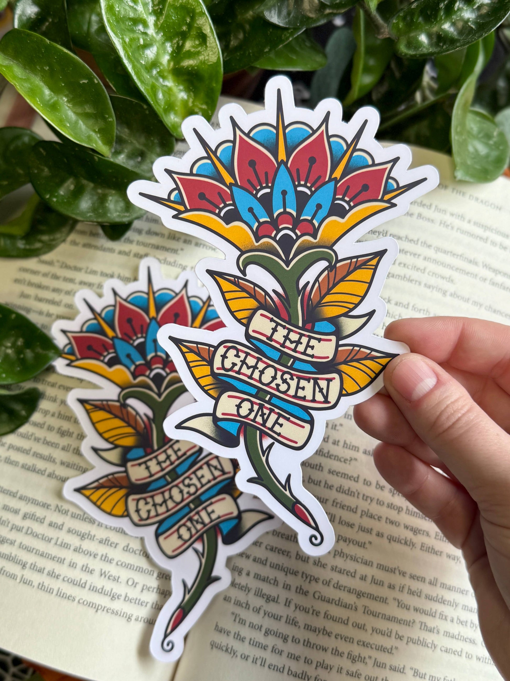 Colorful flower-shaped sticker with 'The Chosen One' text held over a book