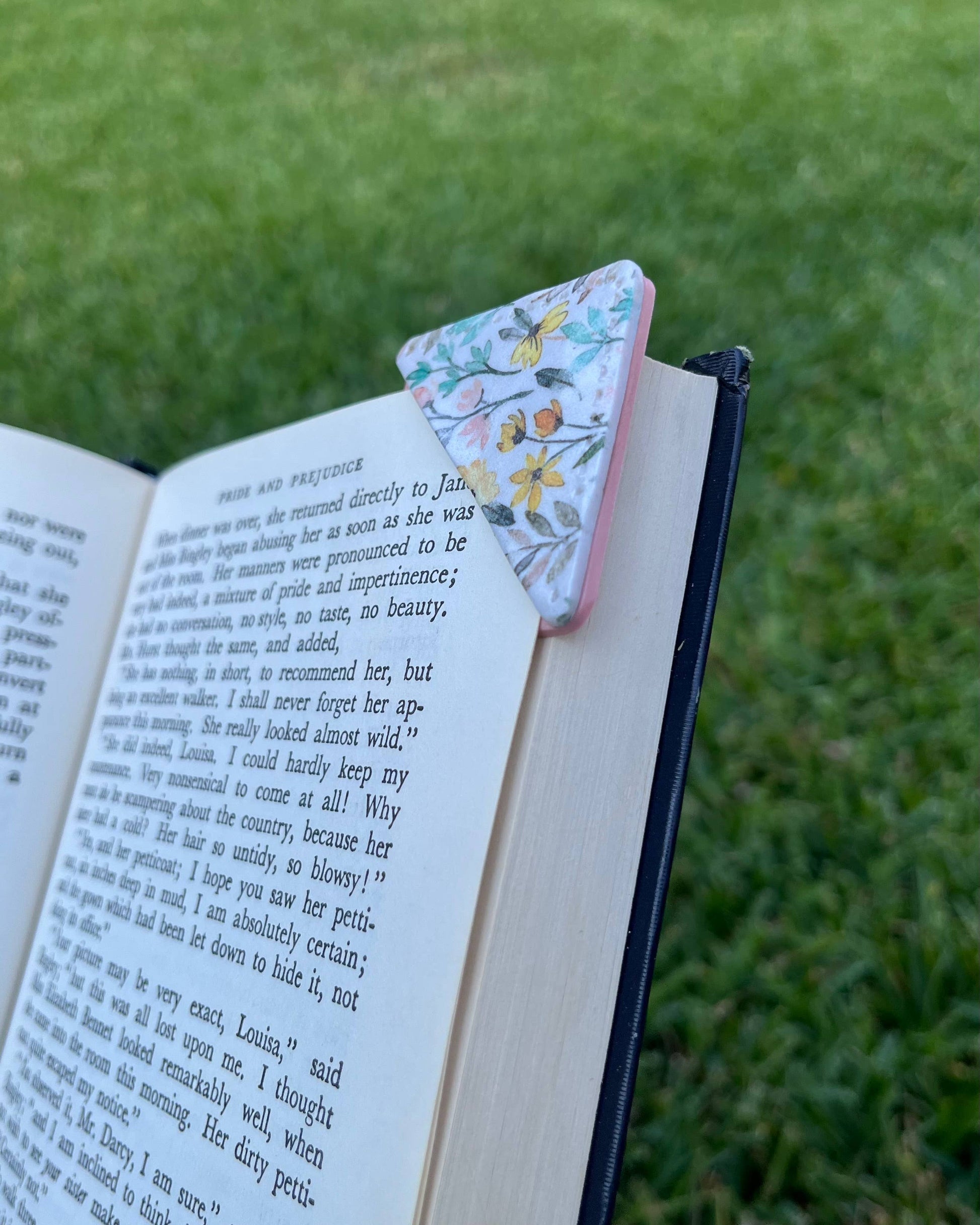 Floral triangle-shaped bookmark on an open book with grass in the background