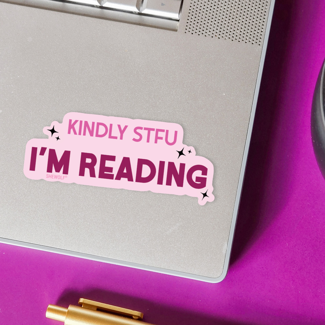 Laptop with a pink sticker reading 'KINDLY STFU I'M READING' on a purple surface.