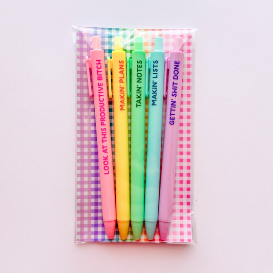 A clear plastic sleeve packaging holds six pastel-colored retractable pens with humorous text printed vertically on them, set against a light pink background.