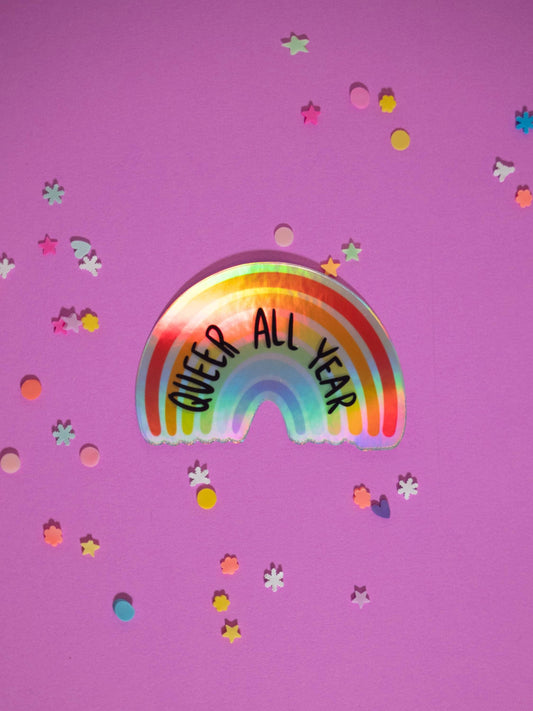 Rainbow sticker with 'QUEER ALL YEAR' text on a purple background with confetti