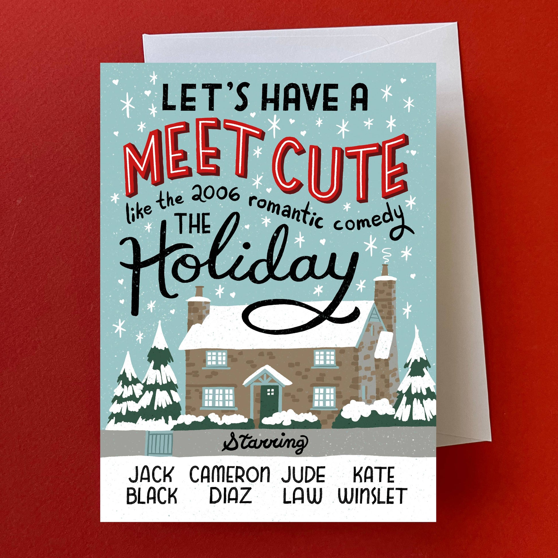 A personalized holiday greeting card with a light blue winter illustration, featuring the text 'LET'S HAVE A MEET CUTE like the 2006 romantic comedy THE Holiday' and a list of names at the bottom. The card is shown with a white envelope against a solid red background.