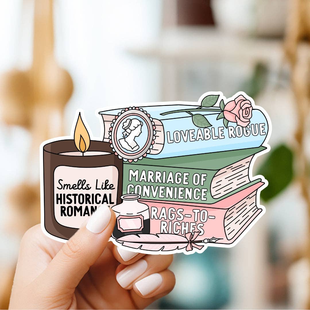 Sticker with book and candle design held by a hand against a blurred background