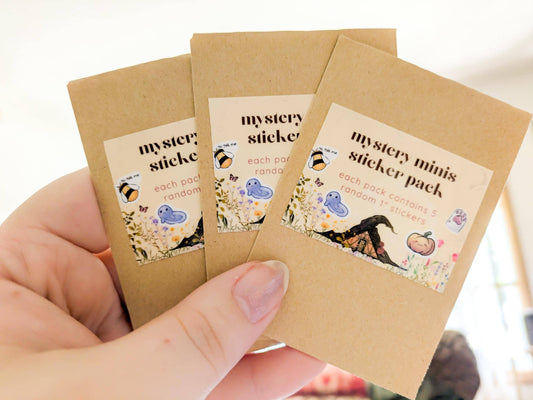 Three brown paper packages labeled 'mystery sticker' held by a hand.