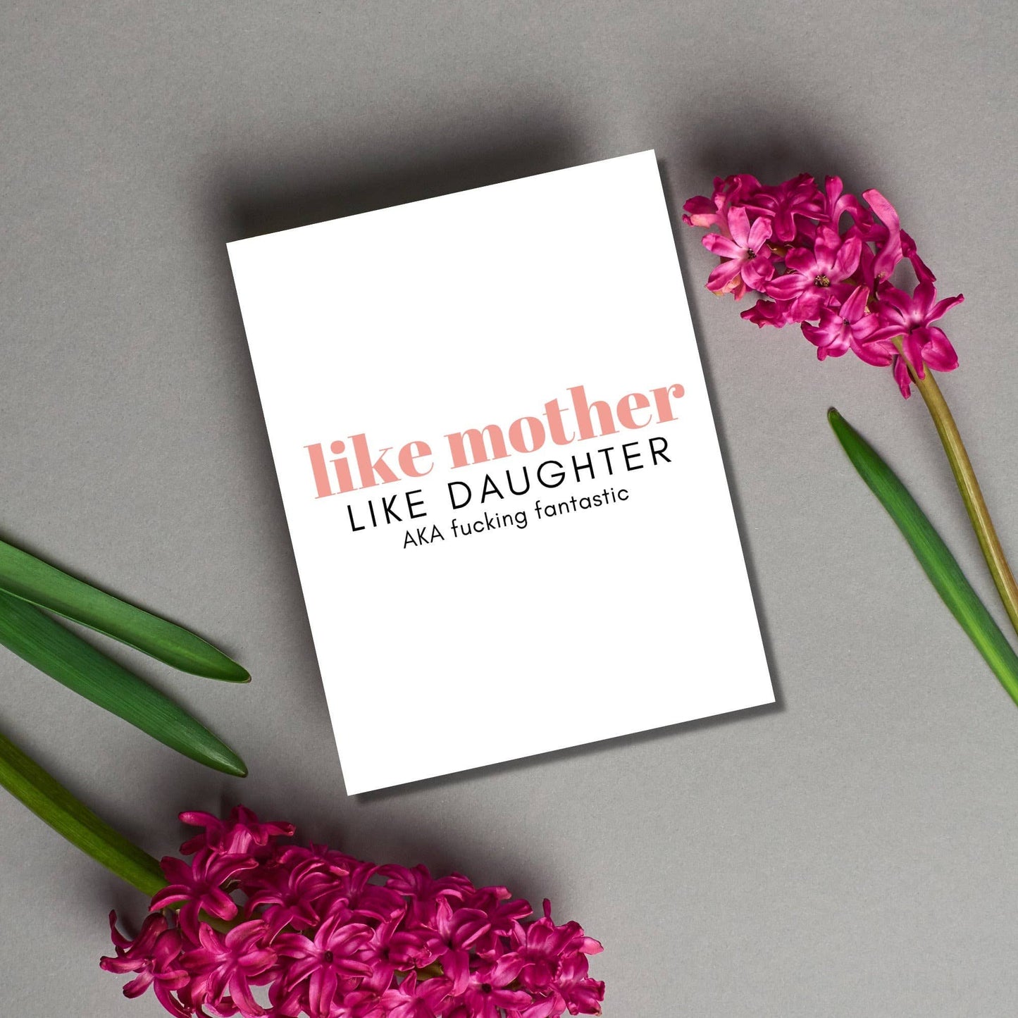 Notebook with 'like mother like daughter' text on a gray surface with pink flowers.