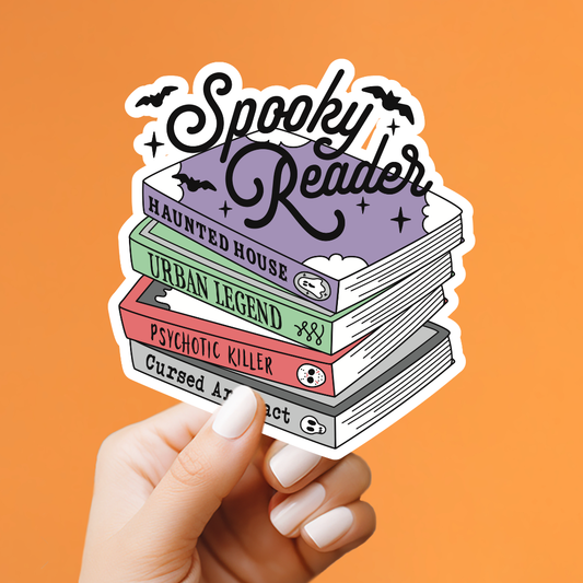 A hand with white manicured nails holds a die-cut sticker featuring a stack of four books with spooky titles and the words 'Spooky Reader' in black script. The background is a solid orange color.