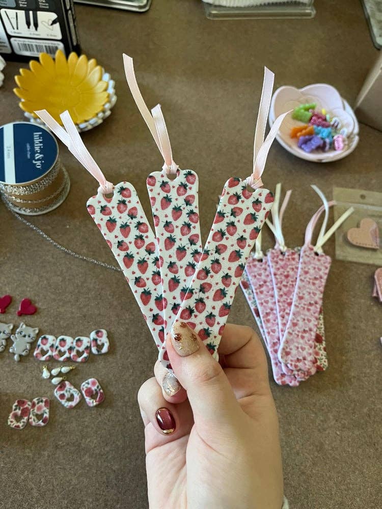 Hand holding decorative clay bookmarks with strawberry pattern on a craft table.
