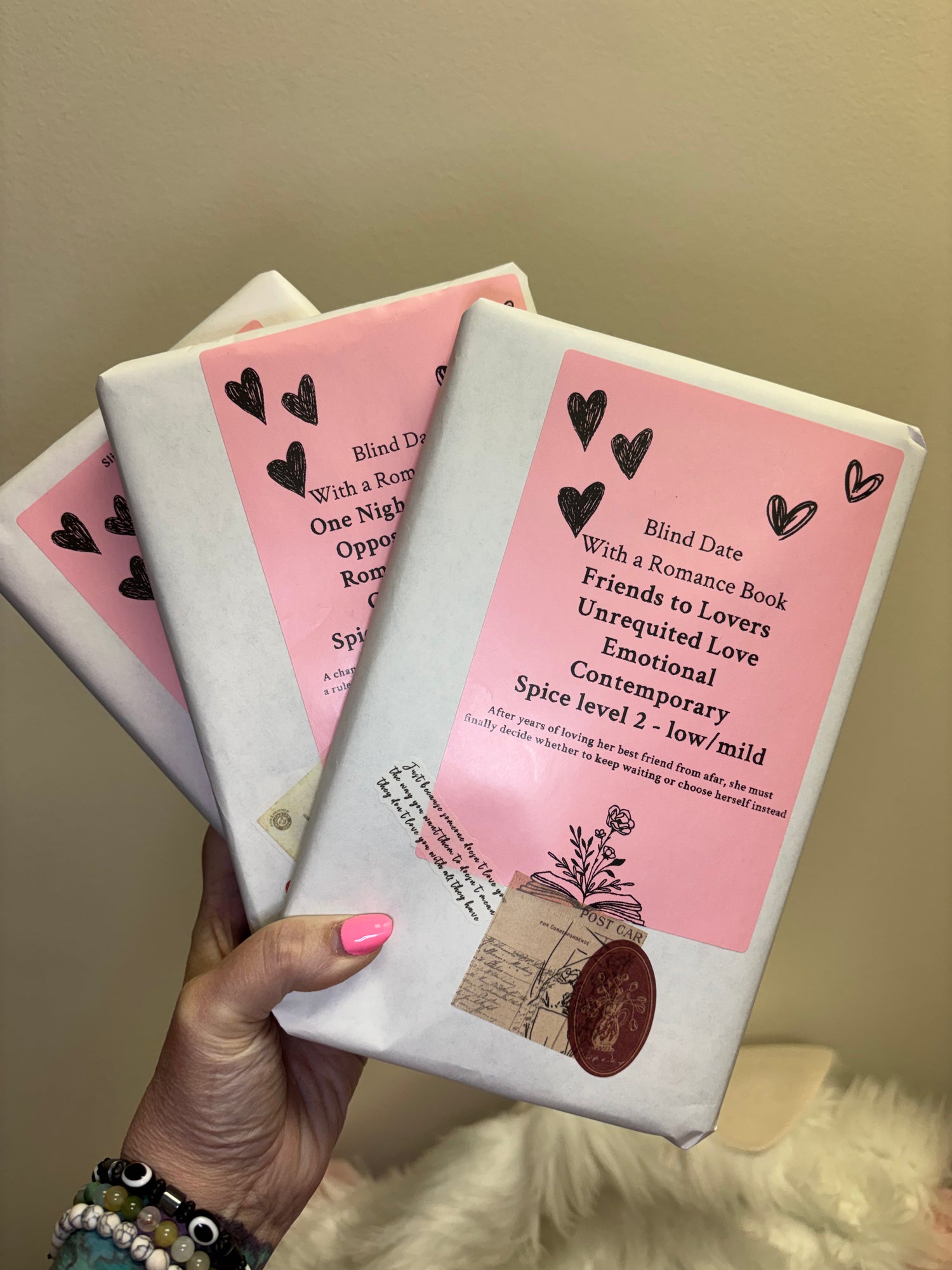 Two books with pink covers held by a hand against a beige background