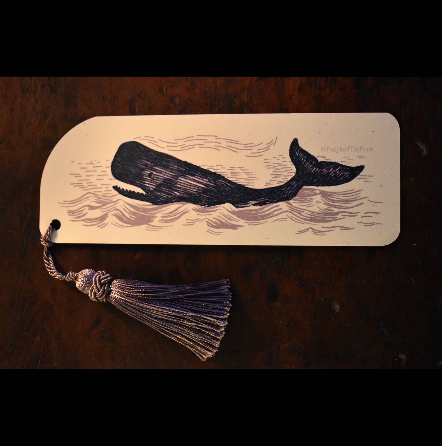 Bookmark with whale design and tassel on a wooden surface