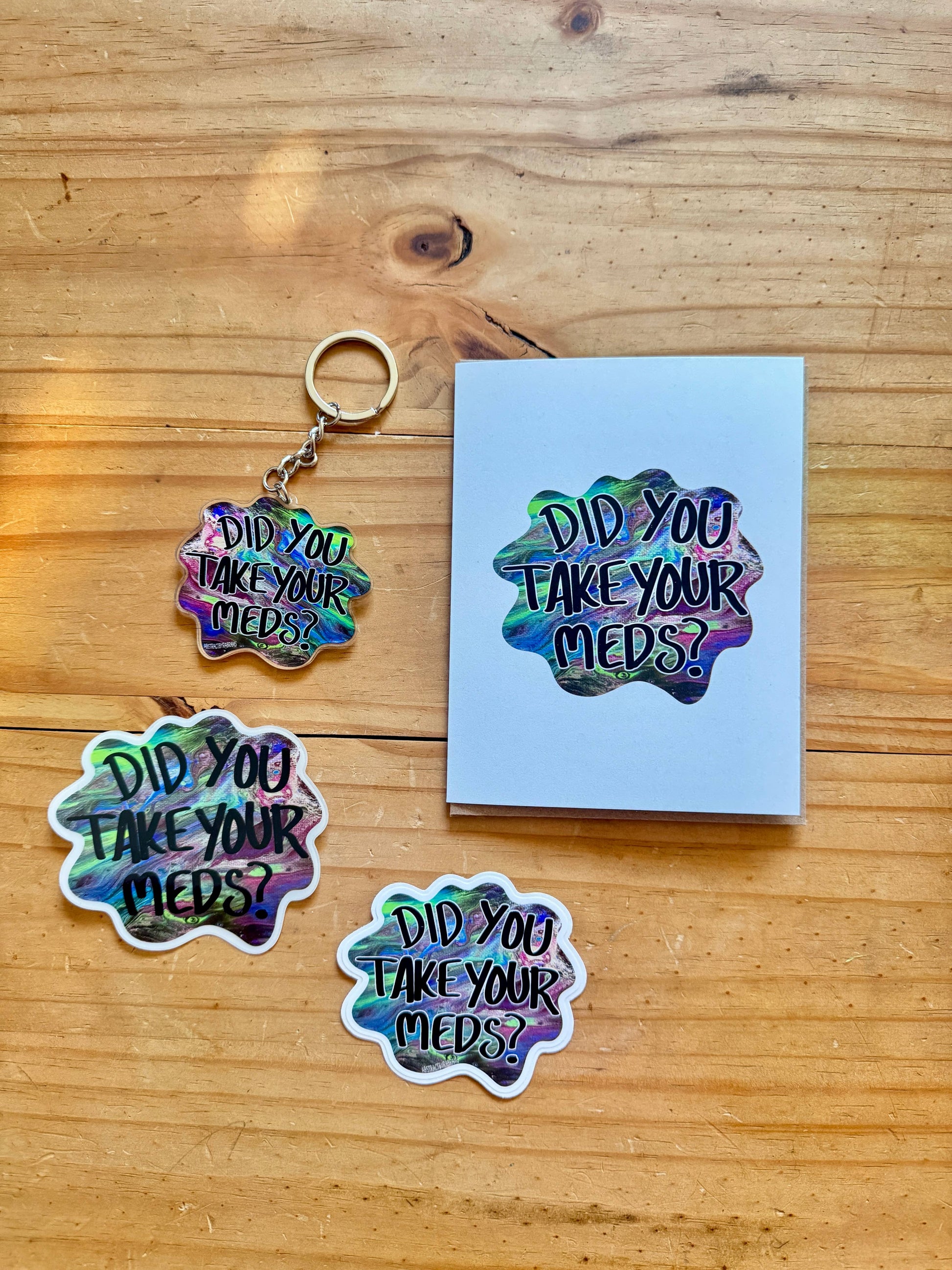 Holographic 'Did You Take Your Meds?' keychain and stickers on a wooden surface