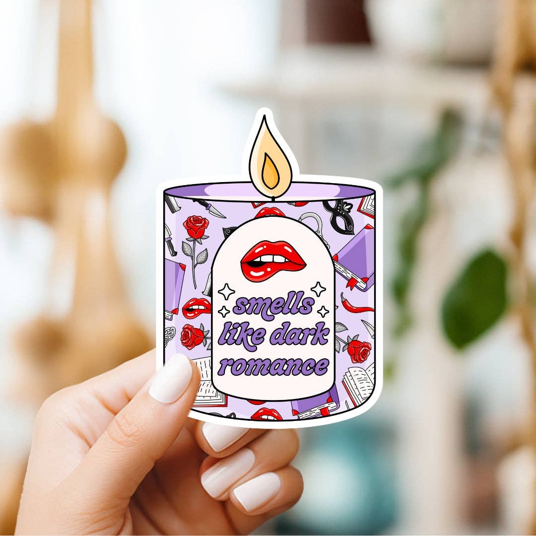 Sticker of a candle with text 'smells like dark romance' held by a hand.