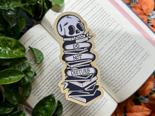 Skull-shaped sticker with 'Do Not Disturb' text on an open book with leaves and pumpkins in the background