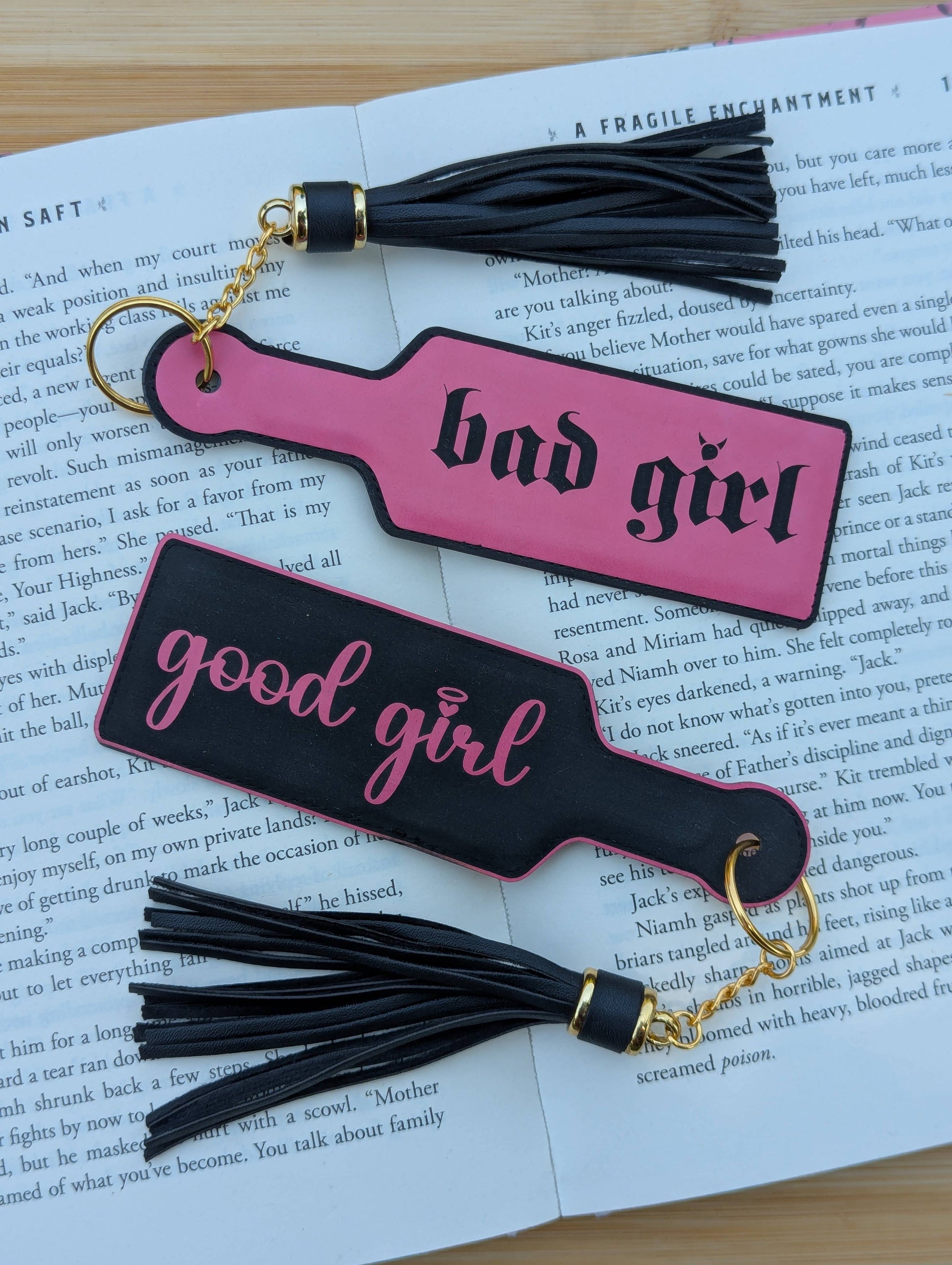 Two pink and black keychains with tassels on an open book.