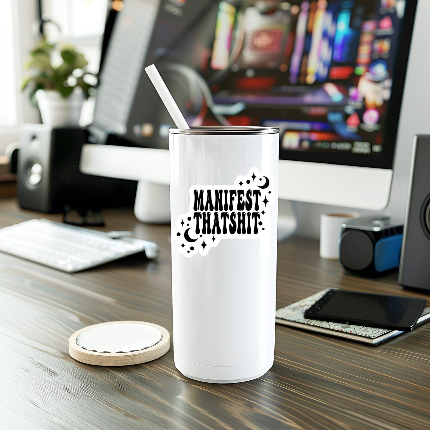 White tumbler with 'Manifest Thatshit' text on a desk with computer equipment.