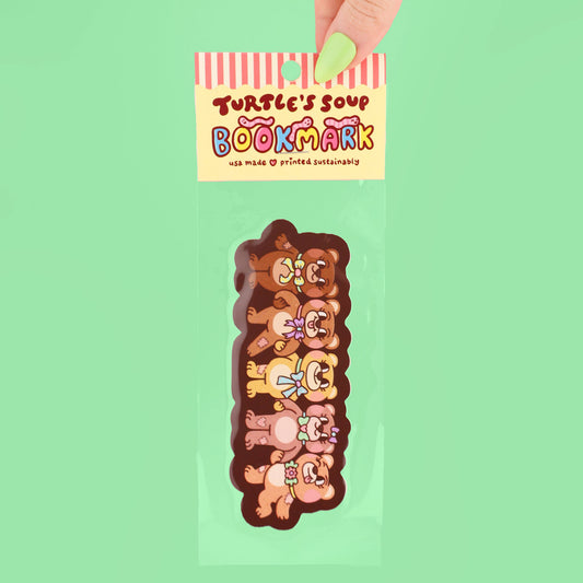 Bookmark with cartoon teddy bear design held by a hand against a green background